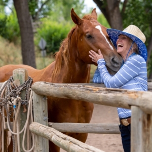 Woman with laughing with horse in stable